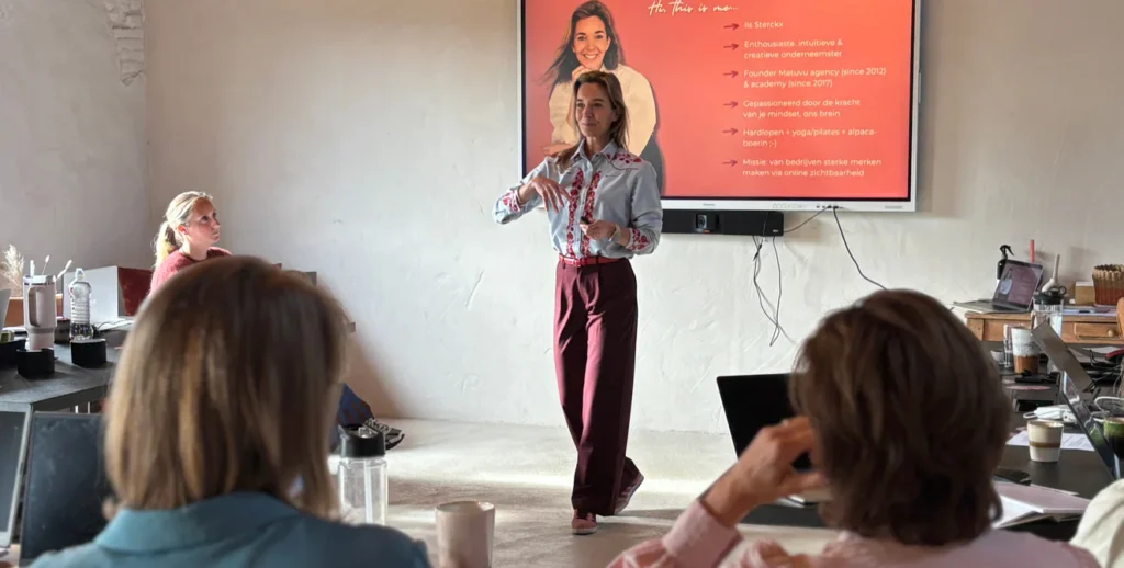 Een vrouw geeft een presentatie aan een groep vrouwen tijdens een welkomstevenement.