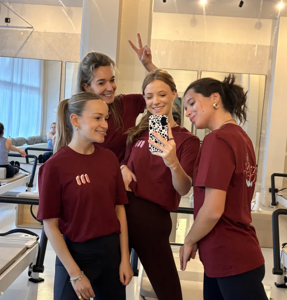Een groep van vier mensen in bordeauxrode shirts poseert voor een spiegel en maakt een selfie.
