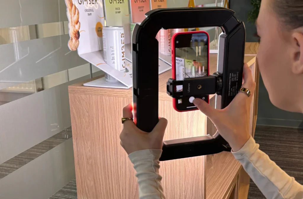 Een vrouw filmt een productdisplay met een smartphone en rig, waarbij GIMBER-producten in beeld zijn.