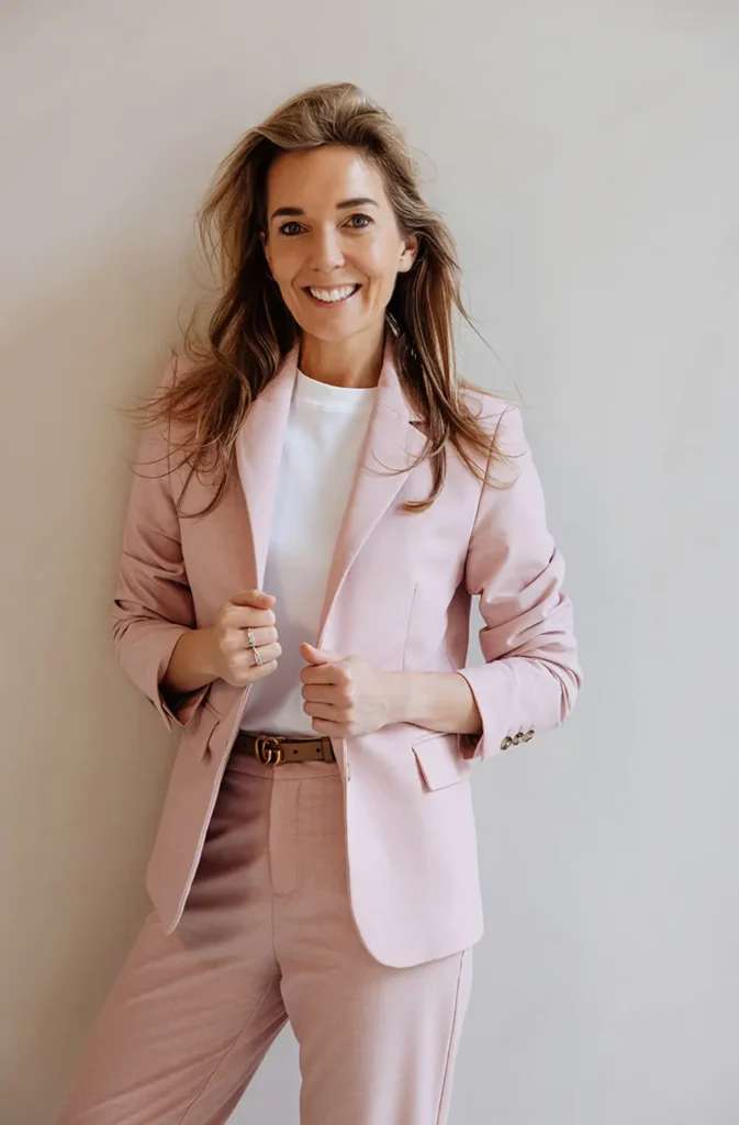 Vrouw in een roze blazer die glimlachend in de camera kijkt.