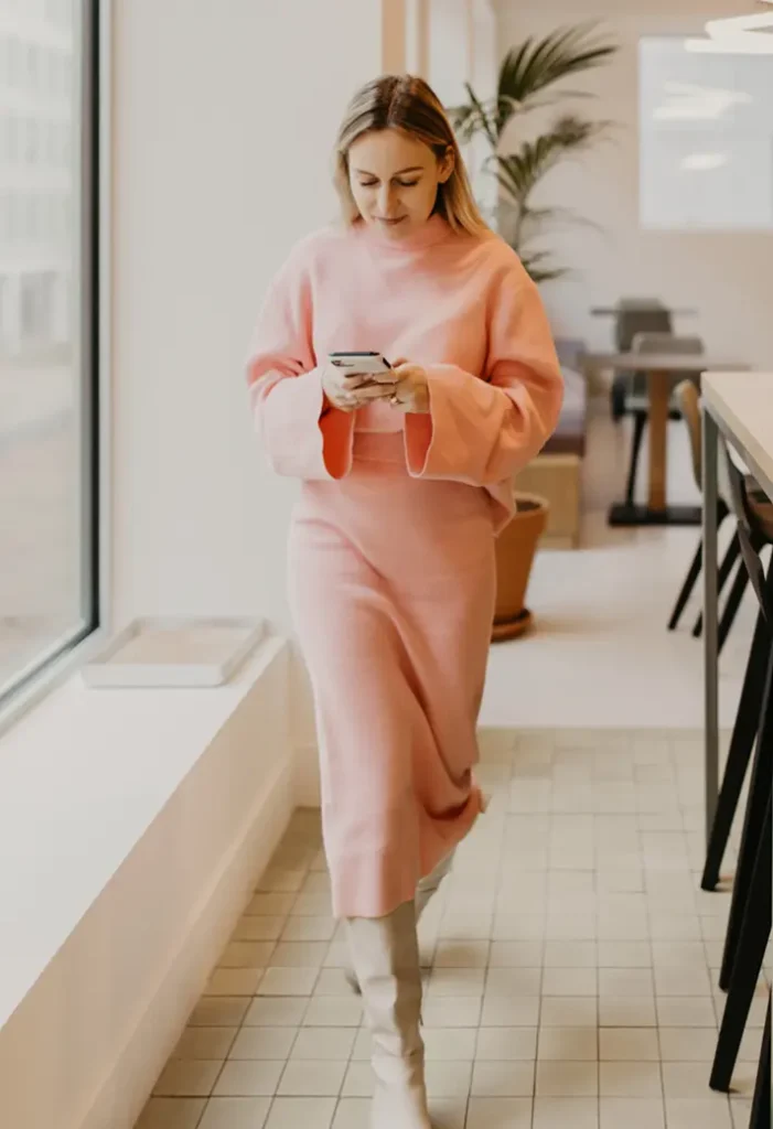 Vrouw in een roze trui loopt binnen en kijkt op haar telefoon.