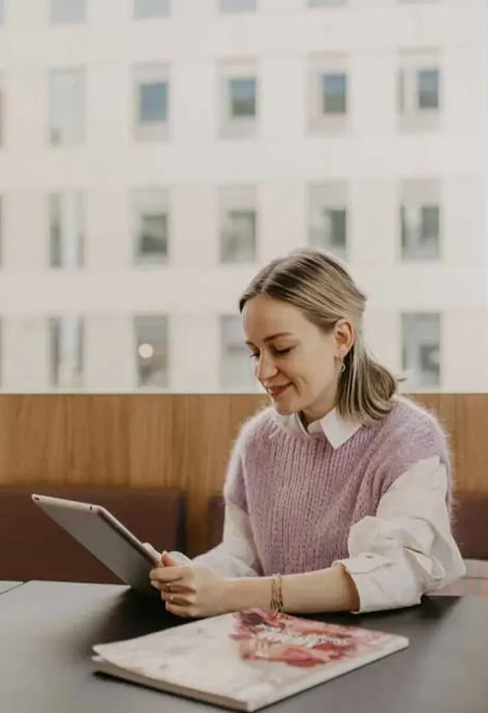Een vrouw zit glimlachend aan een tafel en gebruikt een tablet.