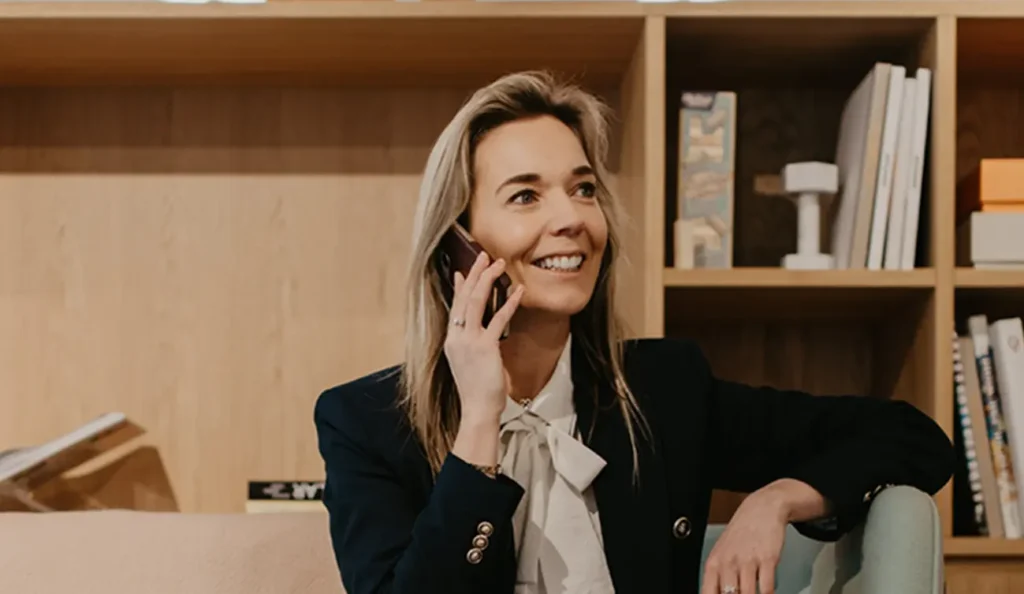 Vrouw glimlacht terwijl ze aan de telefoon zit in een moderne kantooromgeving.