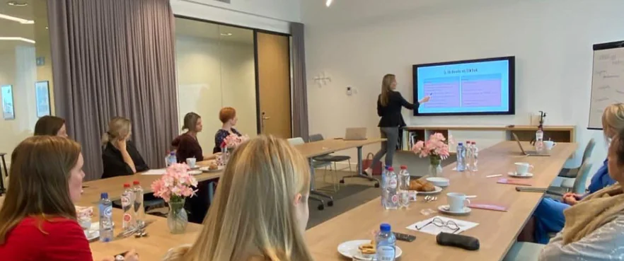 Een vrouw geeft een presentatie aan een groep vrouwen in een vergaderruimte.